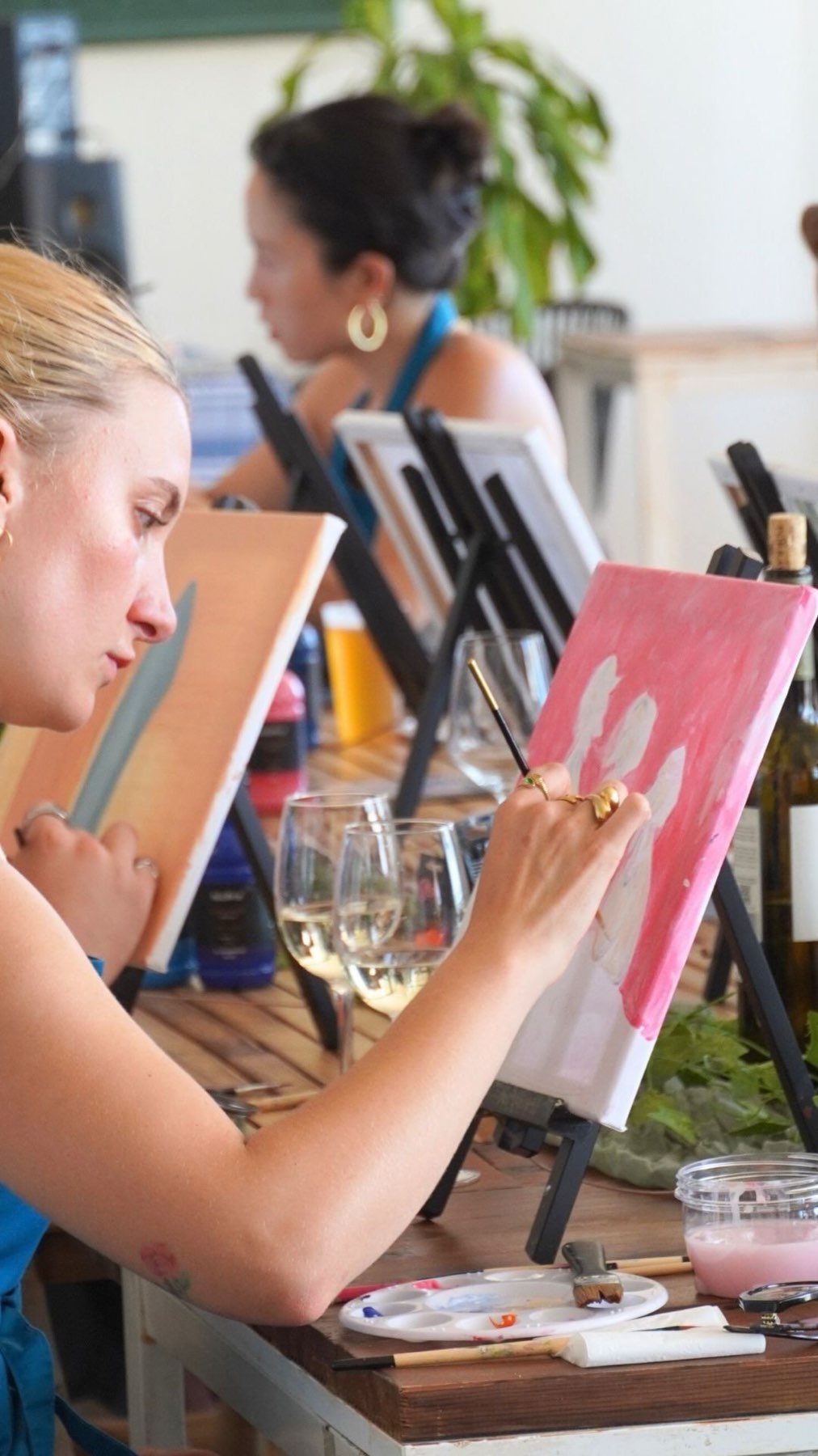 Painters at a table mid-session, hands and wine glasses visible