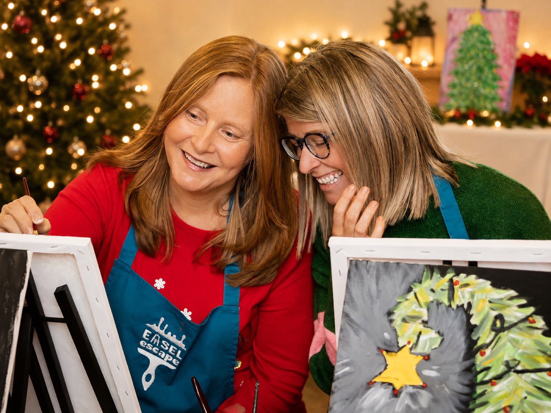 Two friends painting under Christmas tree lights