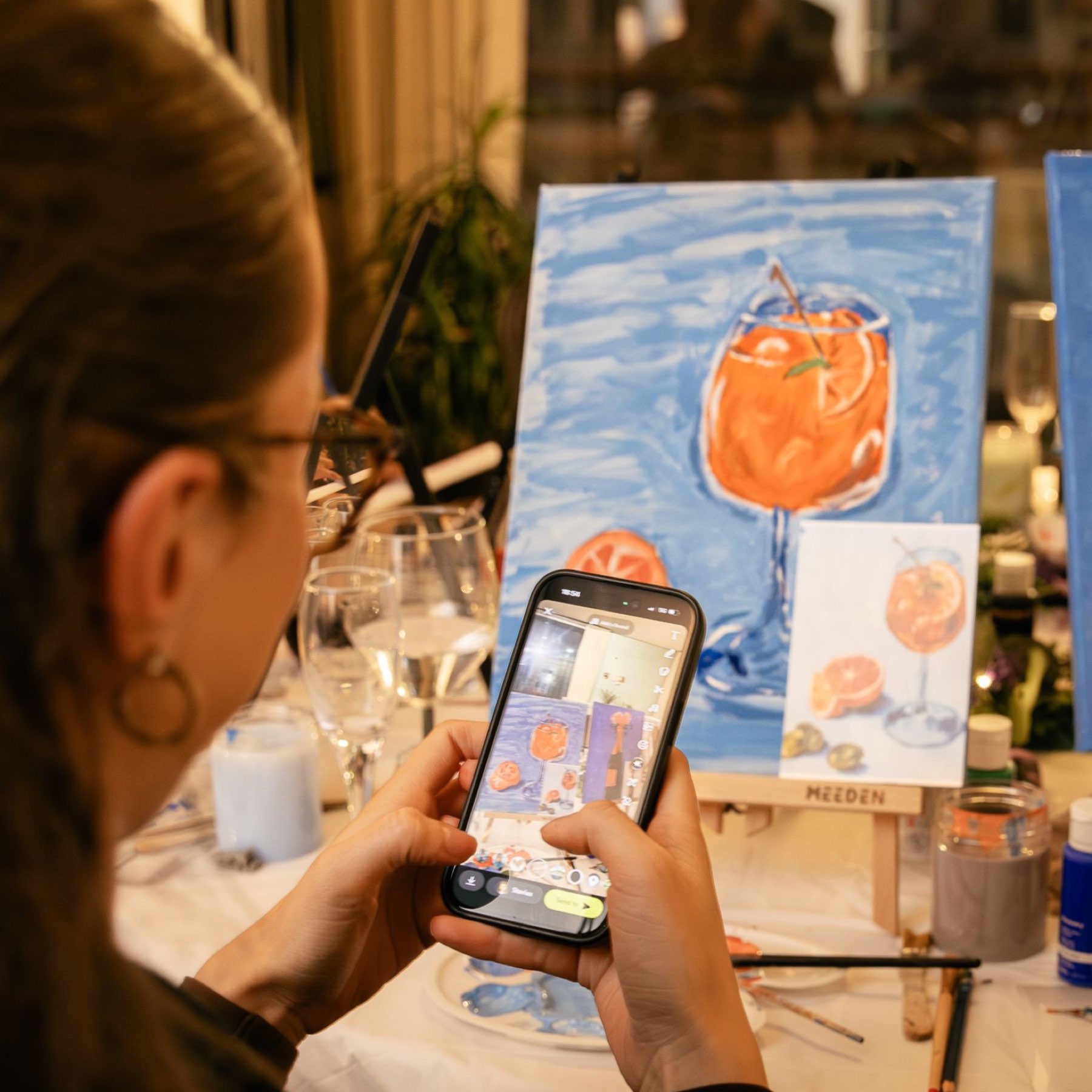 A guest photographing her Aperol spritz painting on her phone to share