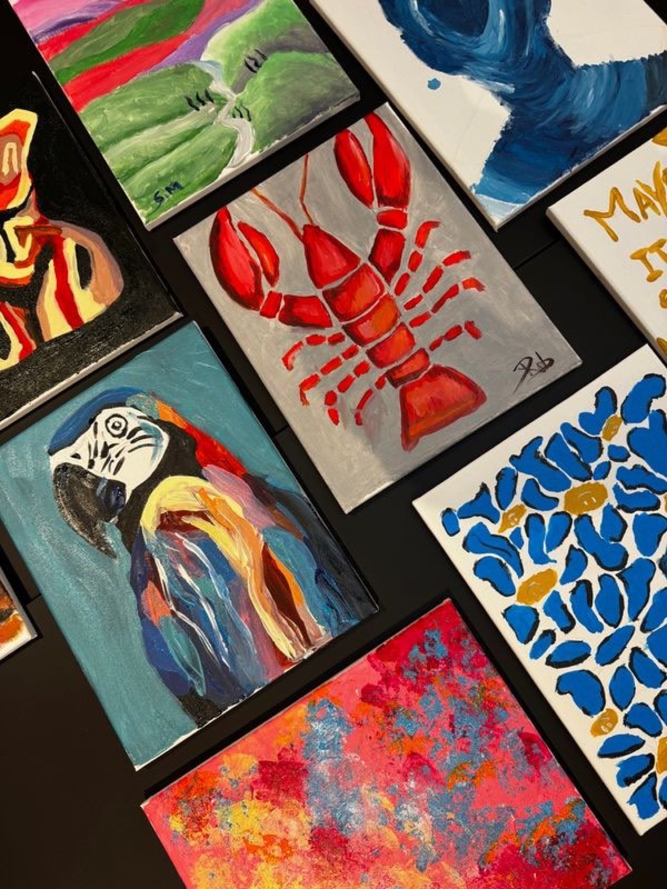 Finished canvases laid out flat: a lobster, a macaw and blue florals