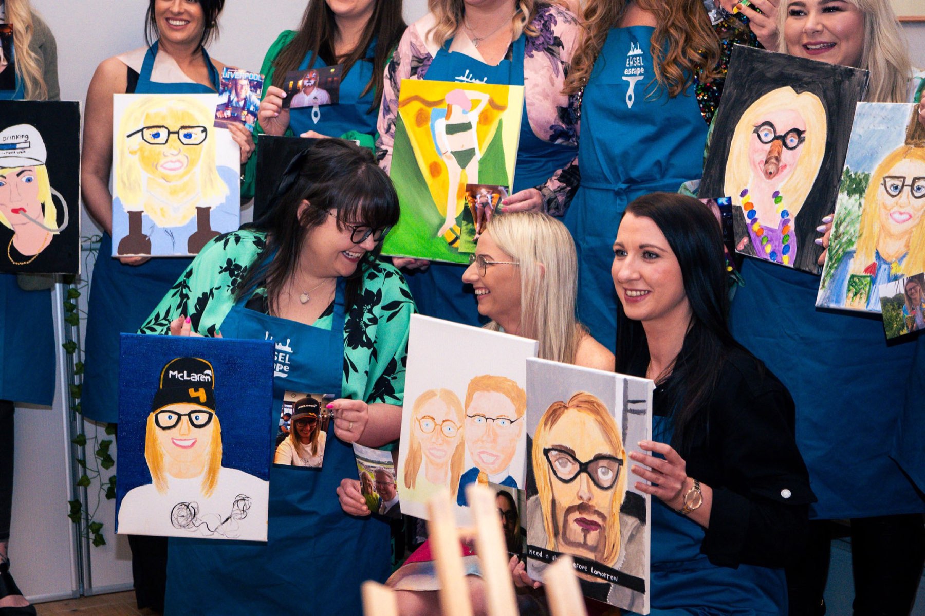 Three guests holding up their finished canvases