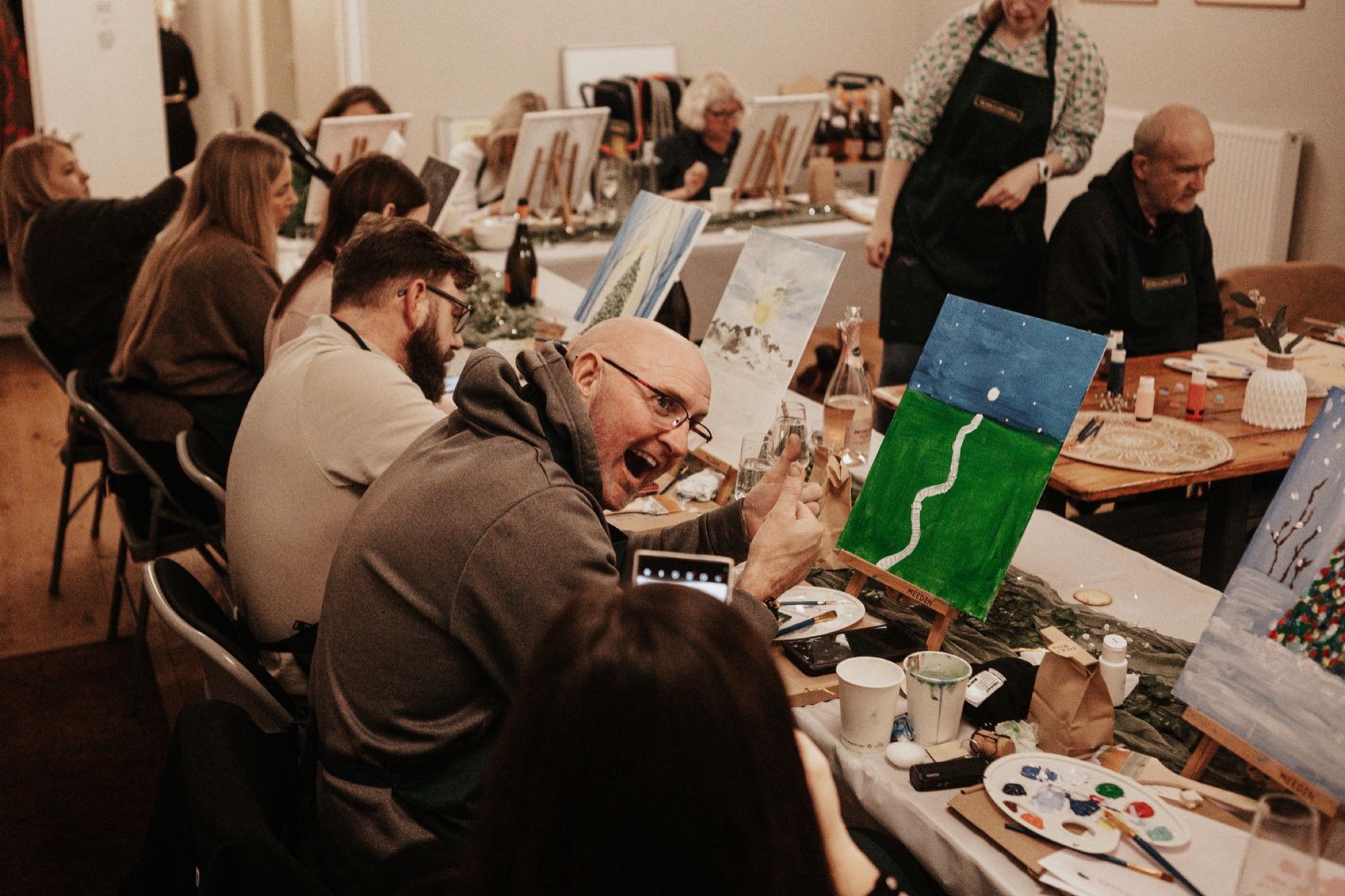 A painter turning round to give a thumbs up beside his canvas