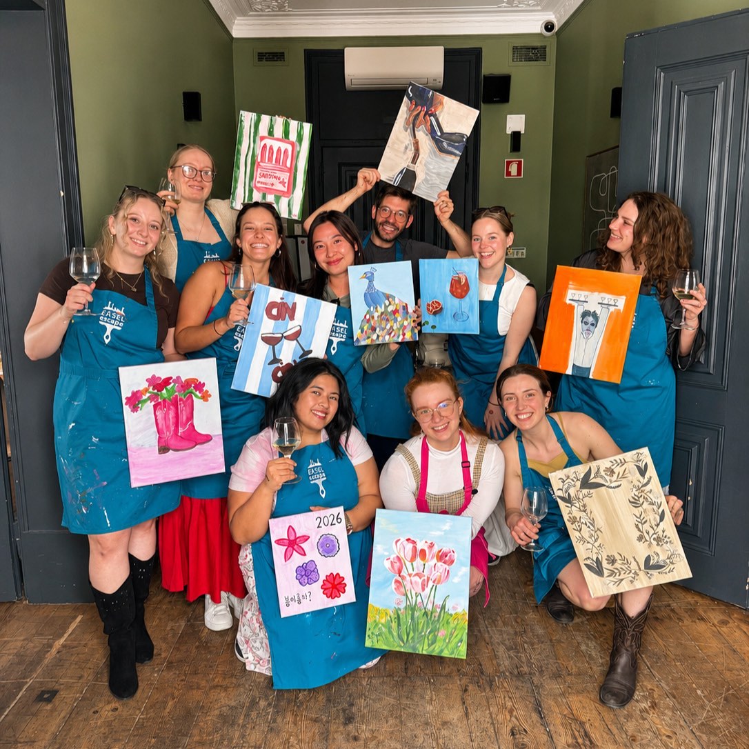 A group of ten painters holding up their finished canvases at a Lisbon paint night