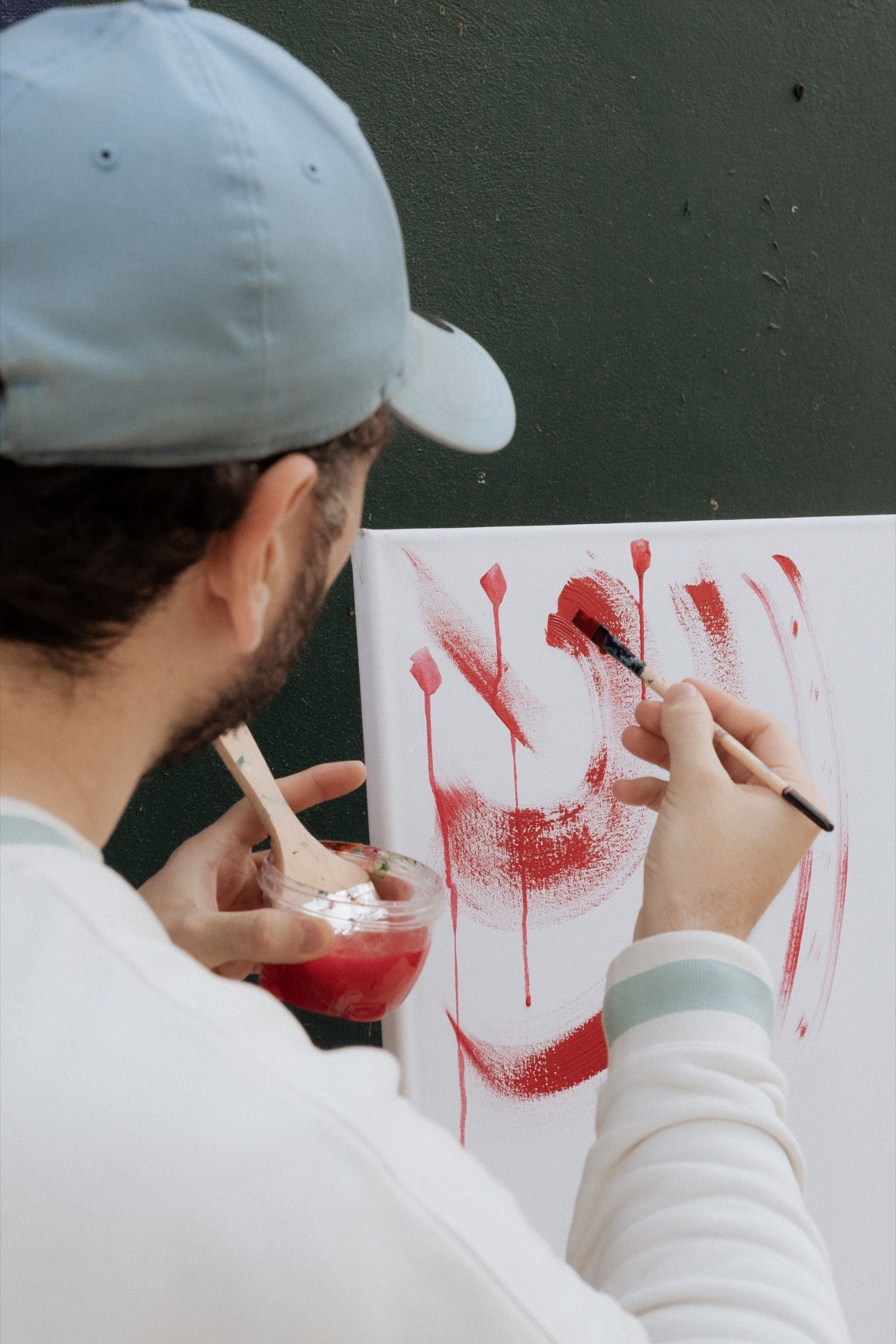 A painter in a cap laying bold red strokes on a canvas